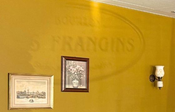 Mur ocre où se devine le logo Les Frangins, cadres et applique ancienne.